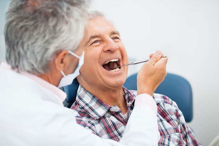 A doctor is checking the teeth of old man